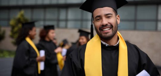 Portrait of a happy graduate student holding his diploma on graduation day and looking at the camera smiling - education concepts