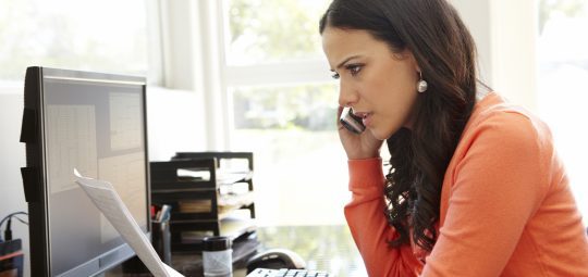 woman on phone reading a letter in front of a computer